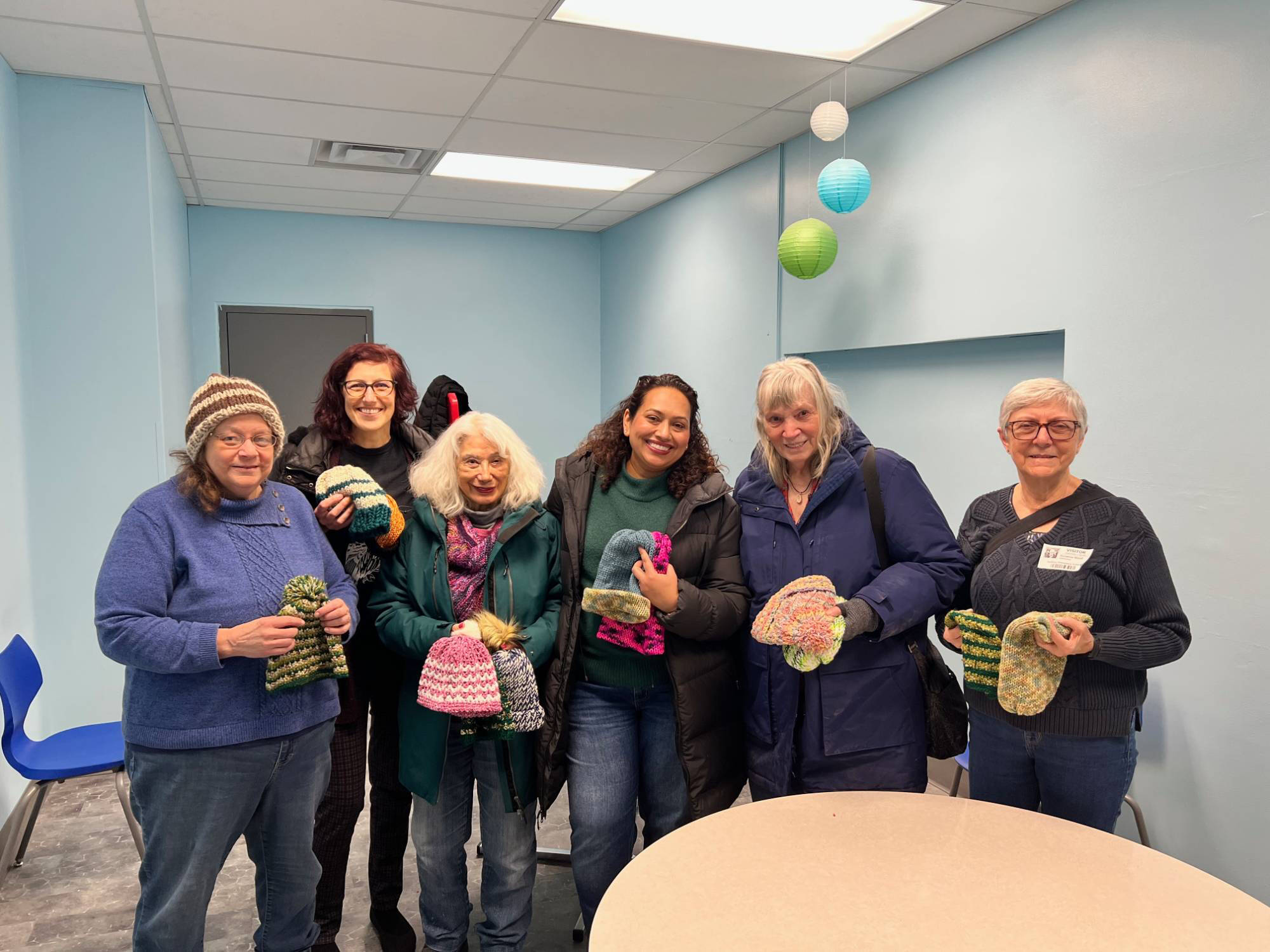 A group of women holding knitted hats.